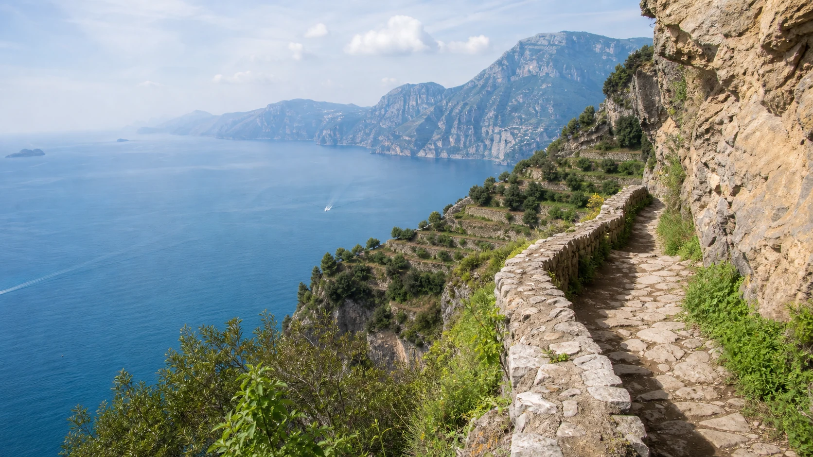 Narrow stone Path of the Gods trail traversing cliffs above the Amalfi Coast with terraced lemon groves and deep blue sea