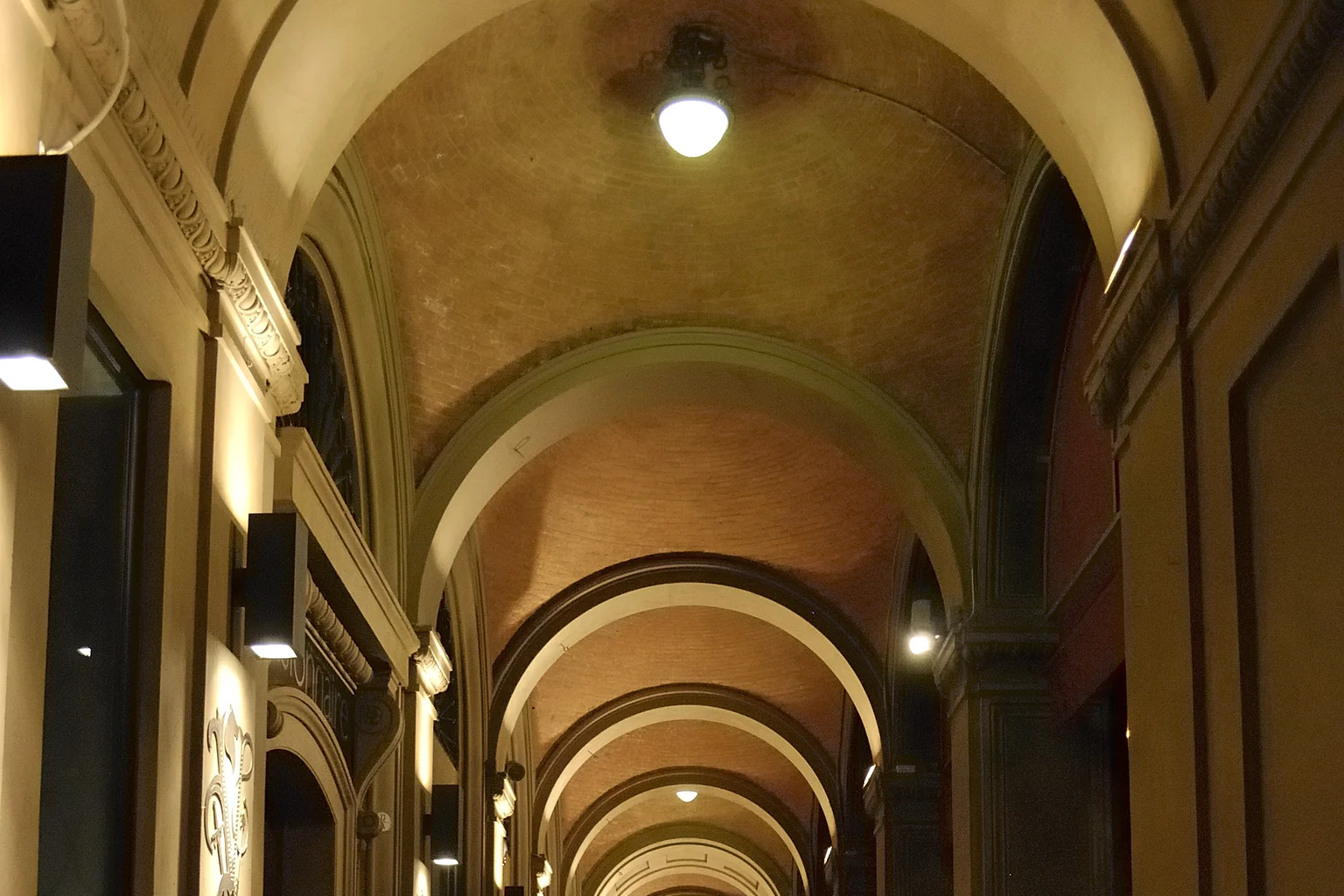 A sequence of warm brick arches beneath Bologna's illuminated porticoes