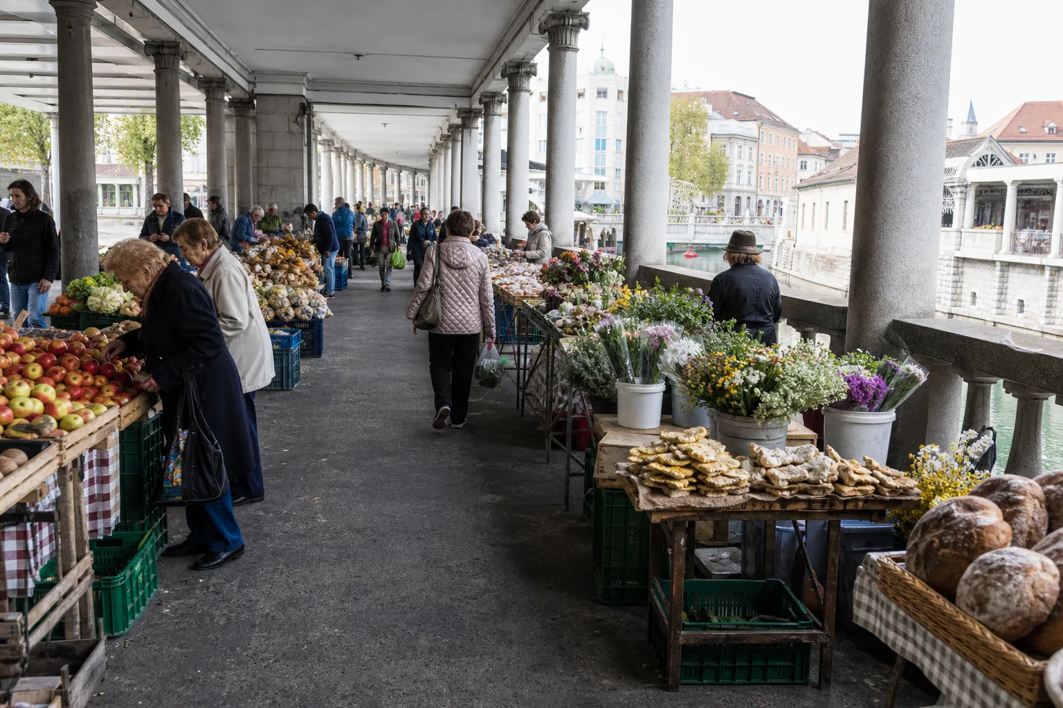 Seasonal produce, bread, flowers, and shoppers beneath the riverside colonnades at Ljubljana Central Market