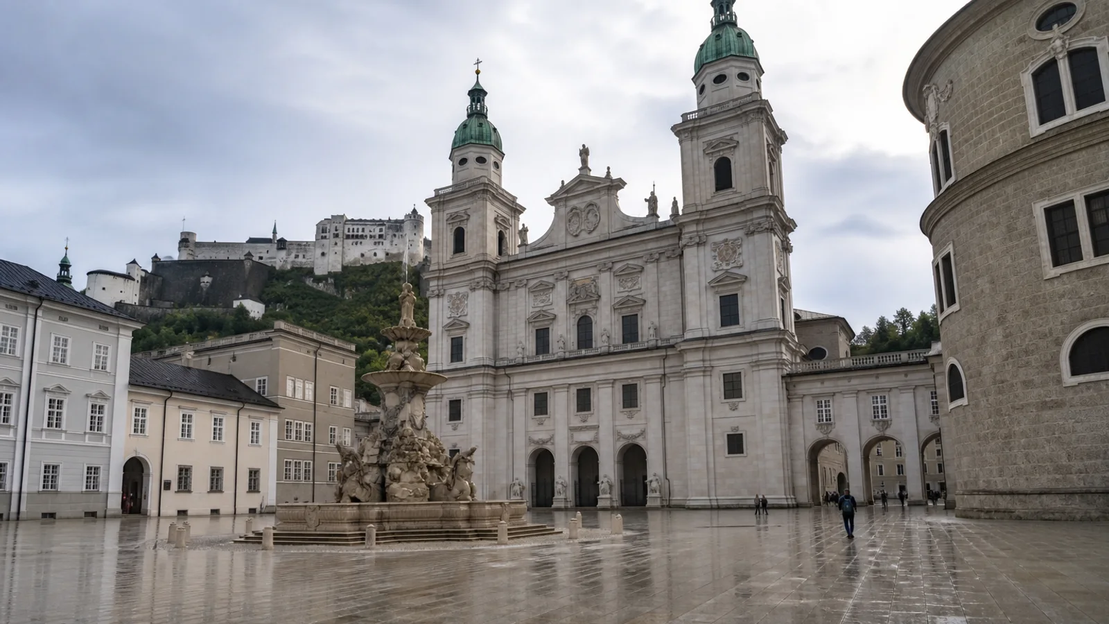 Wet paving on Domplatz in front of Salzburg Cathedral with Hohensalzburg Fortress above